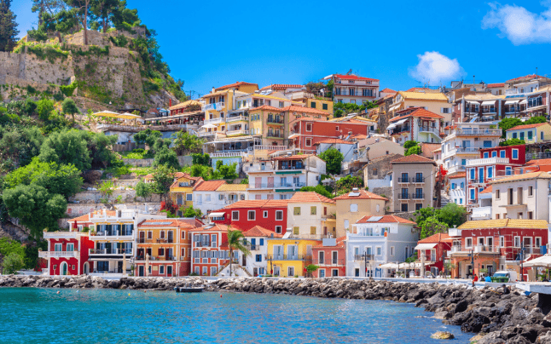 Färgglada hus längs vattnet i Parga, med det venetianska slottet som reser sig på höjden till vänster.